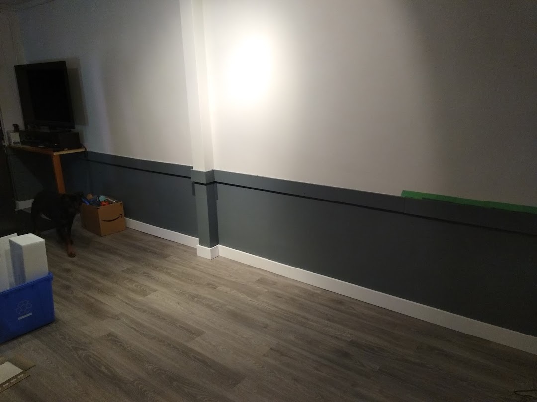 A photo of the new office wall (featuring a two-tone white and dark grey split) and new light grey hardwood flooring. A dog also appears in the corner.